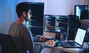 Programista pracuje nad projektem machine learning, pisząc kod na wielu monitorach.