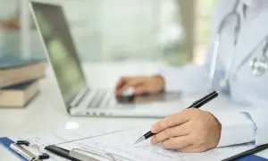 Lekarz wypełnia dokumentację medyczną, korzystając z laptopa i formularza.