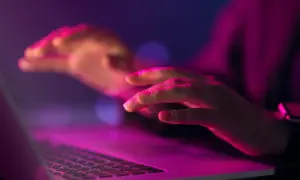 Dłonie nad klawiaturą laptopa w neonowym świetle. Czy to kodowanie, czy szukanie odpowiedzi na pytanie: uuid co to?