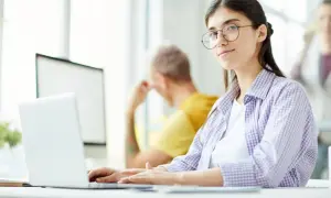 Młoda kobieta w okularach pracuje przy laptopie, szukając ofert pracy jako rpa developer.