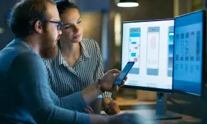 Mężczyzna i kobieta, pracujący jako embedded developerzy, analizują projekt interfejsu aplikacji mobilnej na monitorach.
