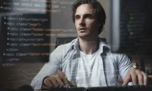 Młody mężczyzna, full stack developer, pracuje przy komputerze, na ekranie widać kod.