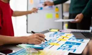 Zespół projektuje interfejsy, planując przyszłe ux designer zarobki. Na stole makiety, palety kolorów i laptop.