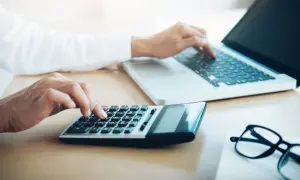 Ręce wpisują dane na kalkulatorze i laptopie, przygotowując się do zakupów e commerce.