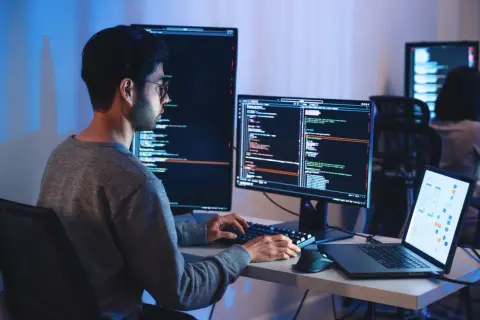 Programista pracuje nad projektem machine learning, pisząc kod na wielu monitorach.