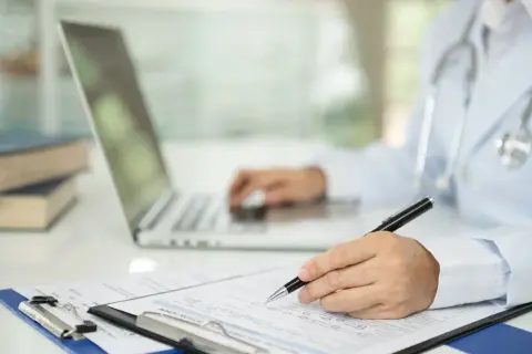 Lekarz wypełnia dokumentację medyczną, korzystając z laptopa i formularza.