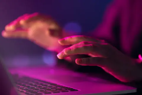 Dłonie nad klawiaturą laptopa w neonowym świetle. Czy to kodowanie, czy szukanie odpowiedzi na pytanie: uuid co to?