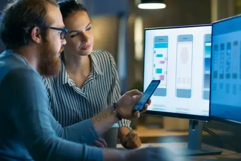 Mężczyzna i kobieta, pracujący jako embedded developerzy, analizują projekt interfejsu aplikacji mobilnej na monitorach.