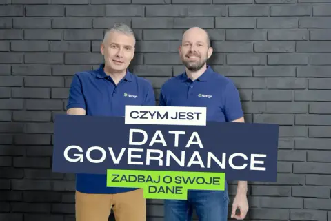 Dwóch mężczyzn w koszulkach z logo Netige prezentuje tablicę z napisem "CZYM JEST DATA GOVERNANCE ZADBAY O SWOJE DANE", podkreślając znaczenie zarządzania danymi.