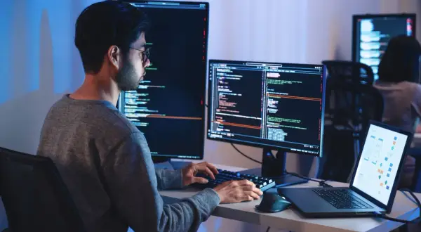 Programista pracuje nad projektem machine learning, pisząc kod na wielu monitorach.