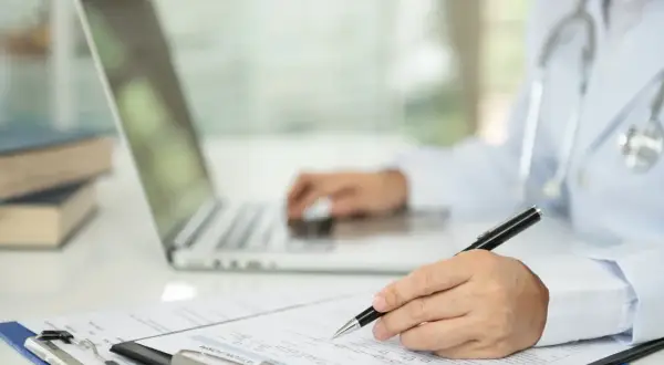 Lekarz wypełnia dokumentację medyczną, korzystając z laptopa i formularza.