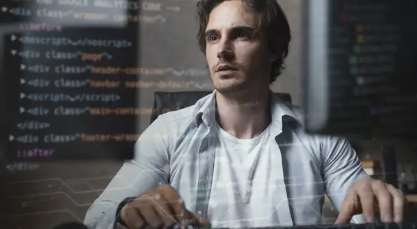 Młody mężczyzna, full stack developer, pracuje przy komputerze, na ekranie widać kod.