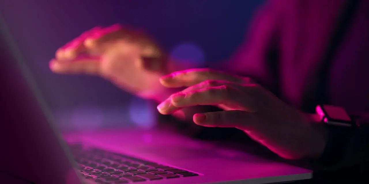 Dłonie nad klawiaturą laptopa w neonowym świetle. Czy to kodowanie, czy szukanie odpowiedzi na pytanie: uuid co to?
