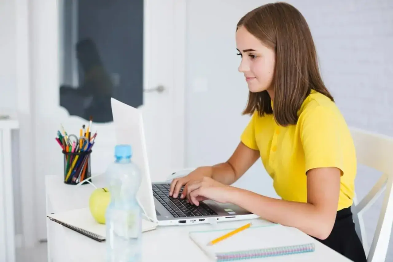 Dziewczyna w ż&oacute;łtej koszulce uczy się programowania na laptopie. To jej pierwszy krok do pracy dla informatyka bez doświadczenia.