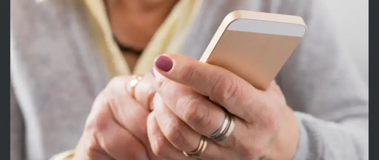 Dłonie z pierścionkami trzymają złoty smartfon. Uważaj na spoofing, czyli podszywanie się pod kogoś w sieci.