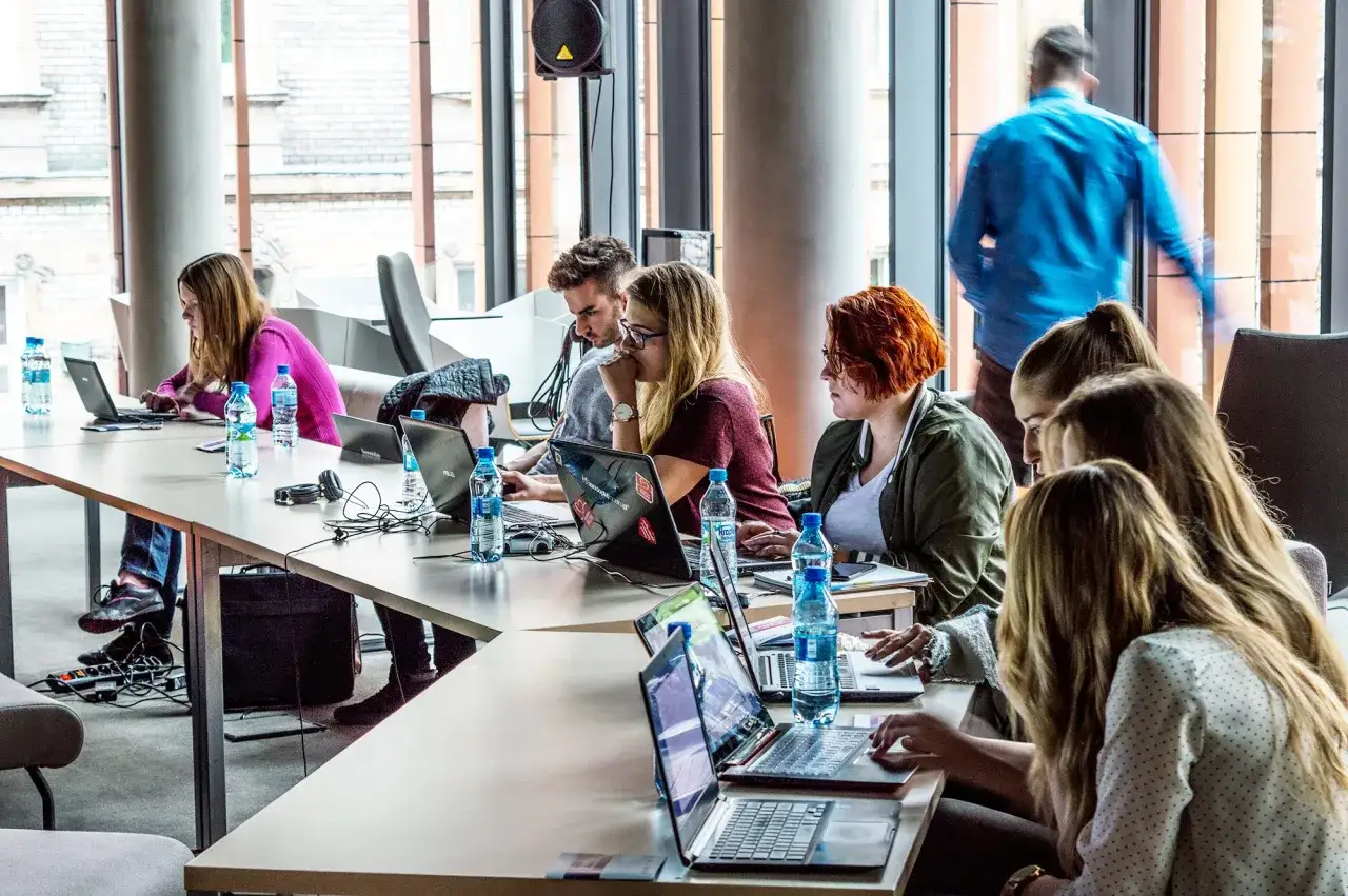 Grupa osób przy biurku, każdy z laptopem, zastanawia się, jaki kurs programowania wybrać.