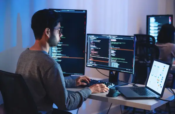Programista pracuje nad projektem machine learning, pisząc kod na wielu monitorach.