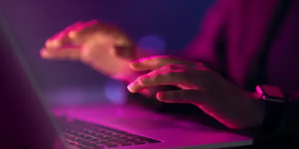 Dłonie nad klawiaturą laptopa w neonowym świetle. Czy to kodowanie, czy szukanie odpowiedzi na pytanie: uuid co to?
