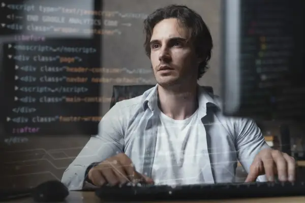 Młody mężczyzna, full stack developer, pracuje przy komputerze, na ekranie widać kod.