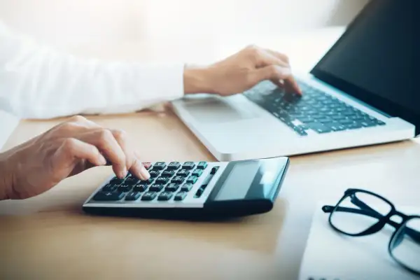 Ręce wpisują dane na kalkulatorze i laptopie, przygotowując się do zakupów e commerce.
